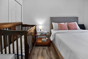 Quarto com berço, mesa de cabeceira com luminária e cama com almofadas.