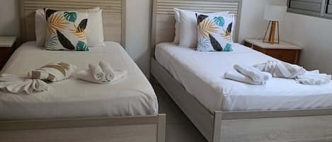 A hotel room with two beds, each with a pillow and rolled towels.