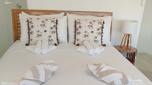 A neatly made bed with towels arranged in a fan shape, a wooden headboard, and a bedside lamp. - Great family holiday home at Magnetic Island where adventure and fun starts. (Nelly Bay)