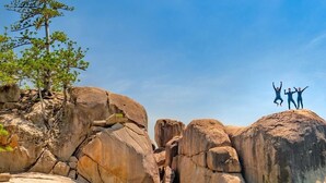 A person paddleboarding in clear turquoise water with large rocks and a tree on the shore. - Great family holiday home at Magnetic Island where adventure and fun starts. (Nelly Bay)