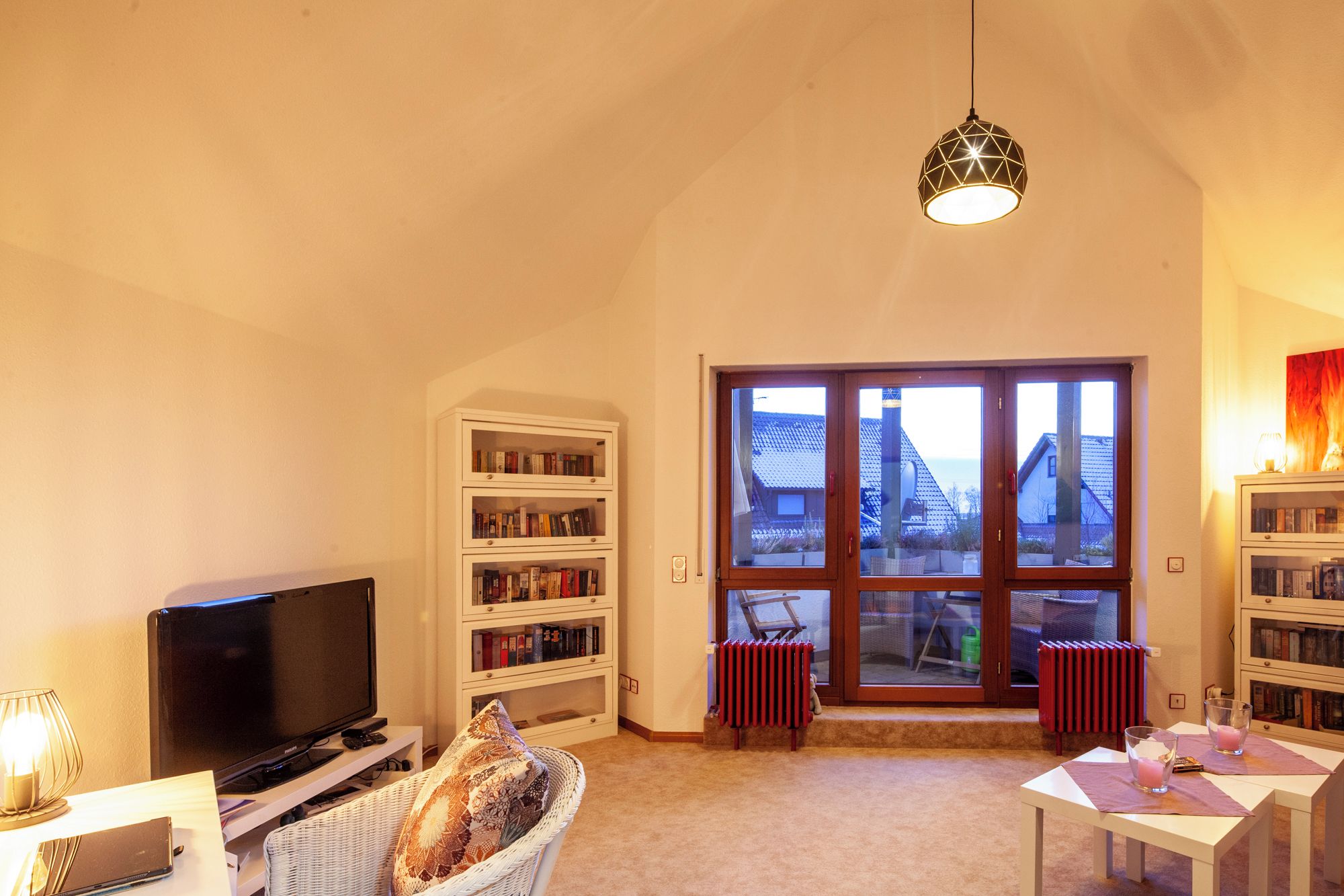 A living room with a television, bookshelves, a window with a view, and a hanging light fixture.