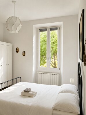 A bedroom with a bed, a window with a view of trees, a radiator, and a white wardrobe. - Room-natures Retreat - Private Room - N (Florence)