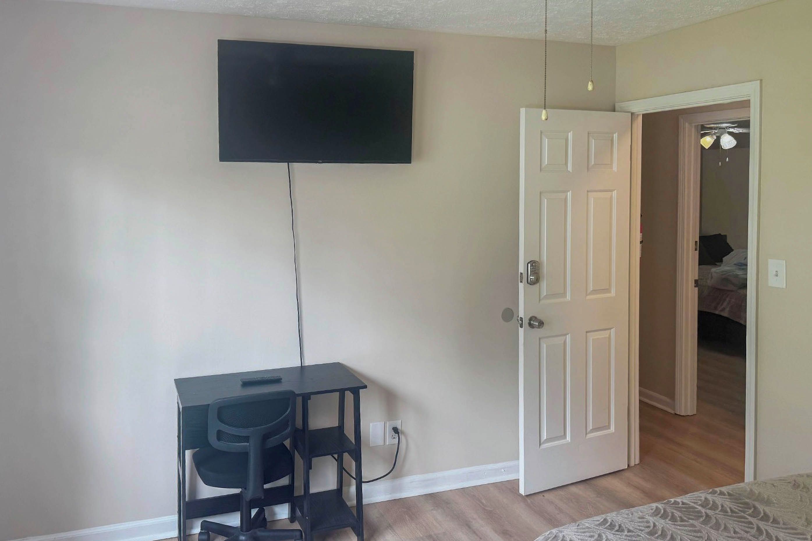 A room with a desk, chair, and a television mounted on the wall.