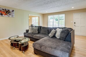 A living room with a sectional sofa, a glass coffee table, and hardwood flooring. - Kennesaw Home Near KSU & Lake Acworth (Kennesaw)