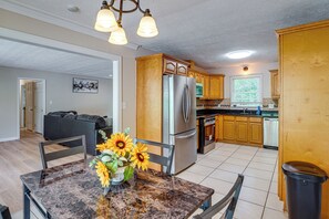 A modern kitchen with wooden cabinets, stainless steel appliances, and a dining area with a marble table and sunflowers. - Kennesaw Home Near KSU & Lake Acworth (Kennesaw)