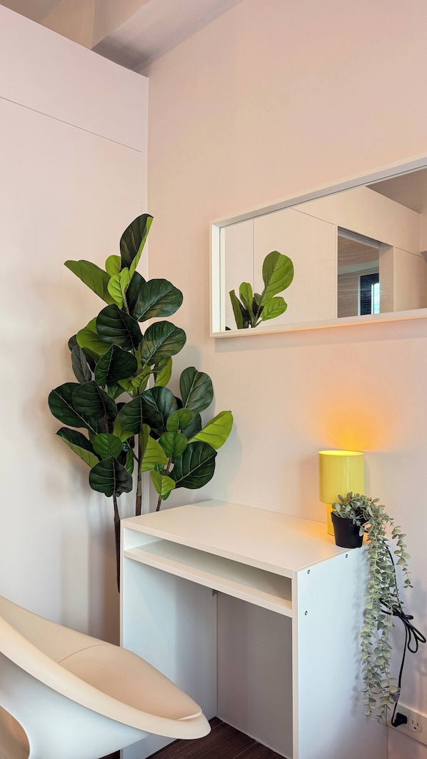A white desk with a mirror above it, a yellow lamp, and a potted plant.