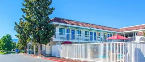 A motel with a swimming pool, covered outdoor seating, and a fenced area.