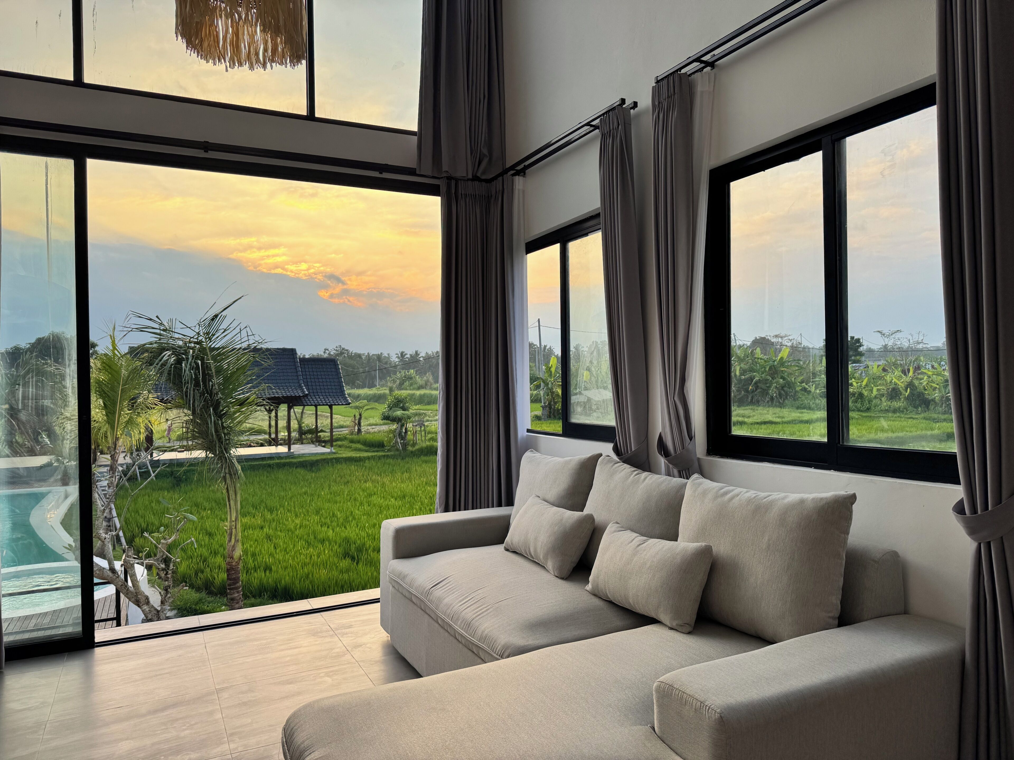 A modern living room with a large window, a sofa, and a view of a swimming pool and greenery.