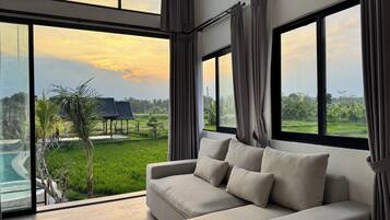 A modern living room with a large window, a sofa, and a view of a swimming pool and greenery.