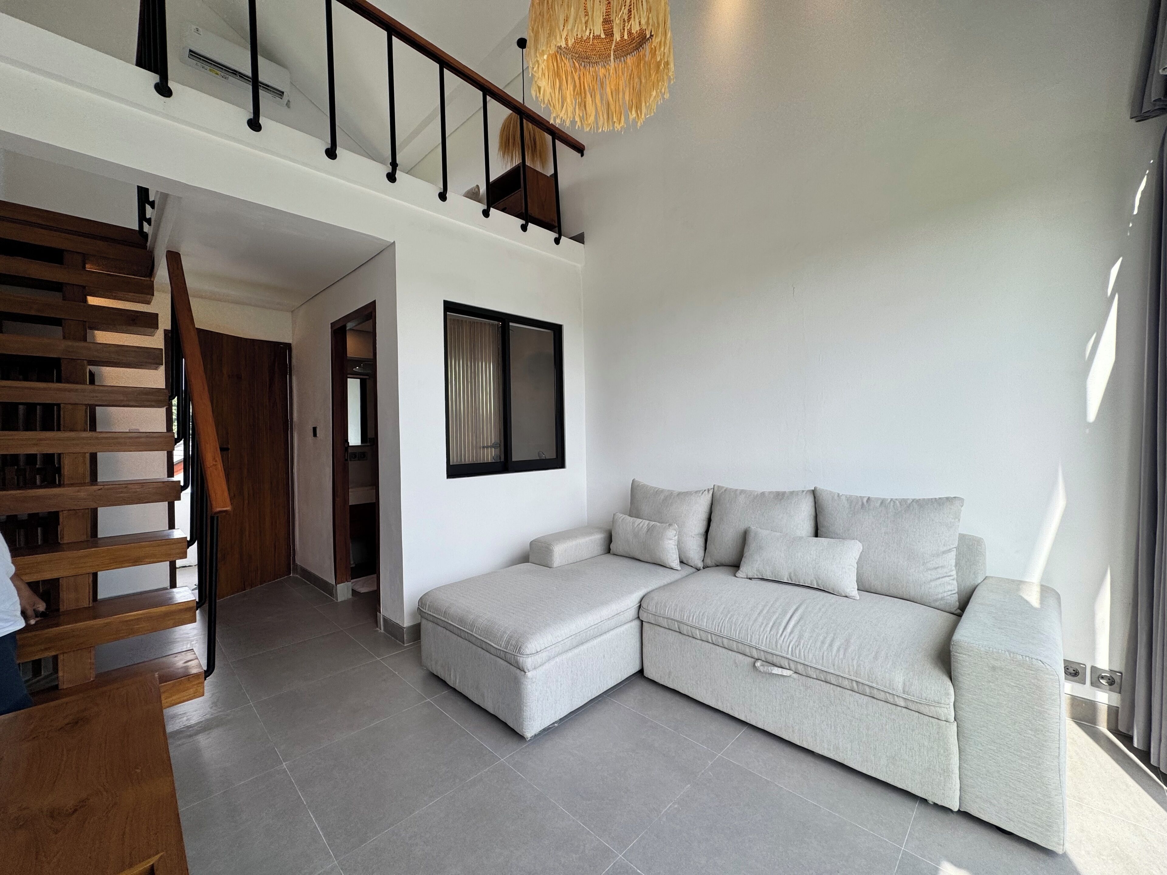 A modern living room with a grey sectional sofa, a wooden staircase, and a large window.
