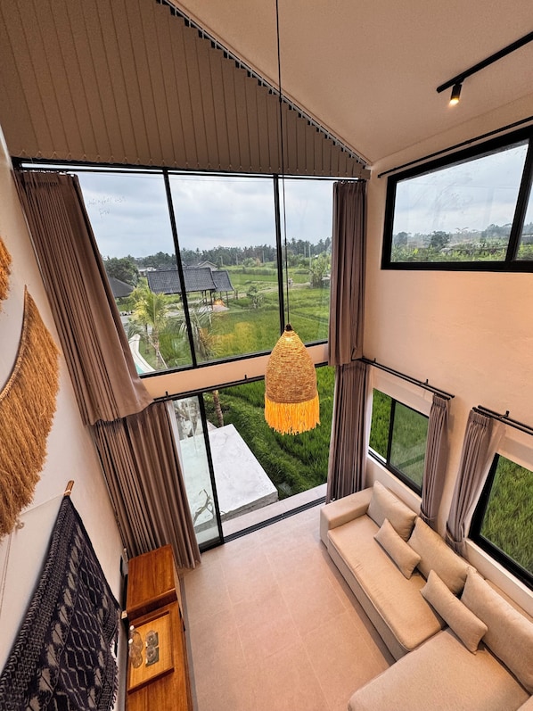A modern interior with large windows, a hanging light fixture, and a sofa.