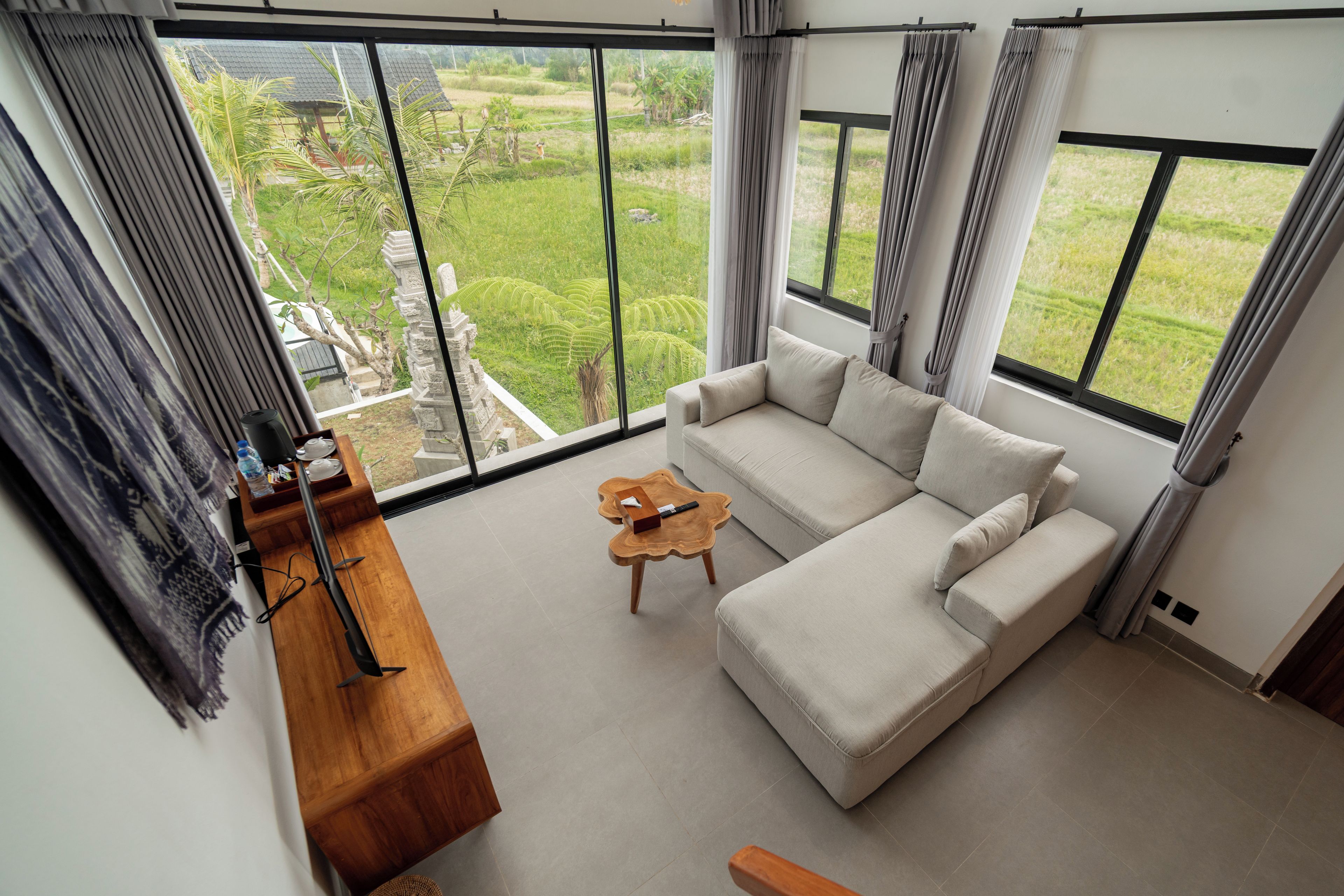 Ein modernes Wohnzimmer mit einer Couch, einem Couchtisch und Blick auf einen üppigen Garten durch große Fenster.