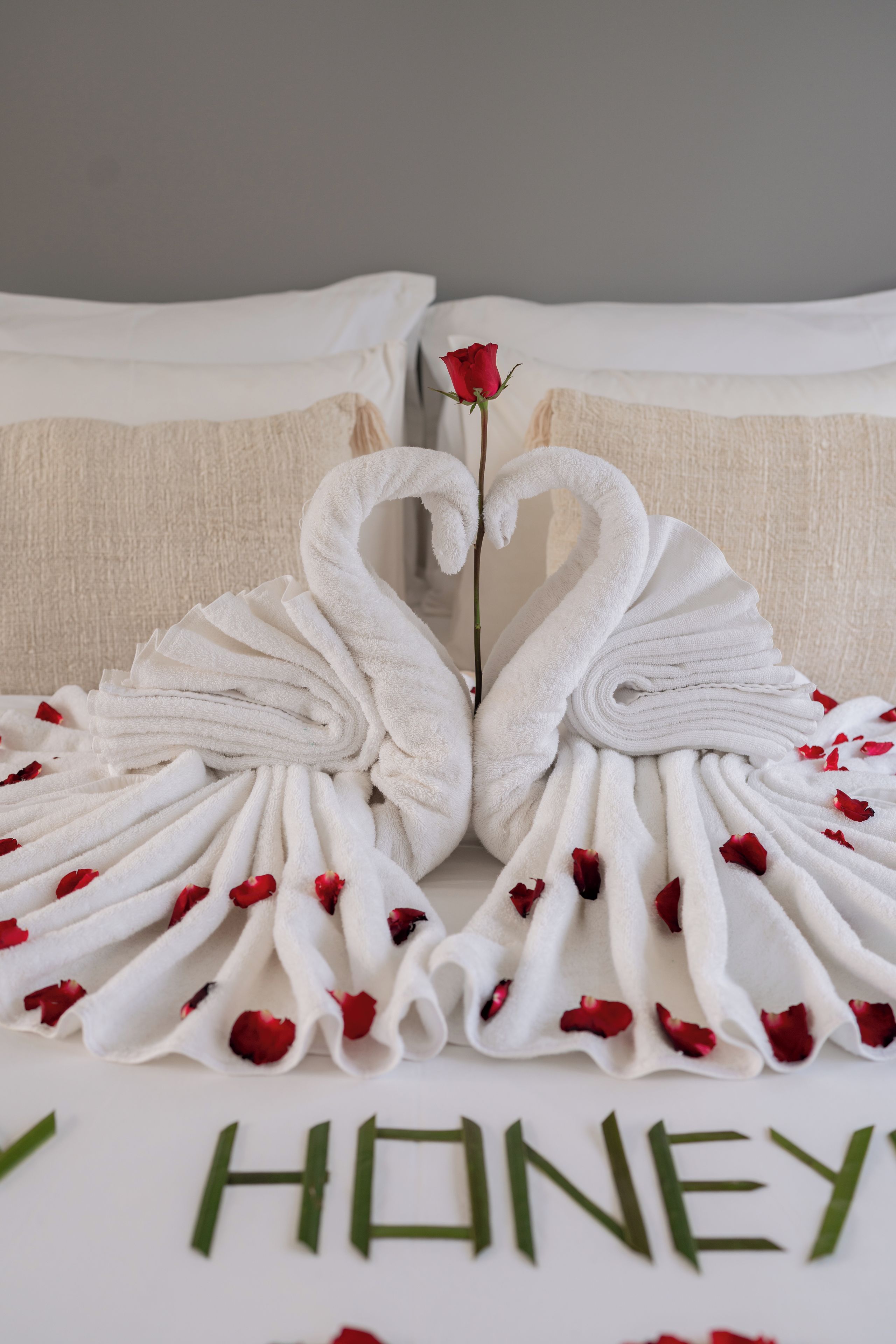Un lit avec du linge de lit blanc et une serviette pliée en forme de cœur.