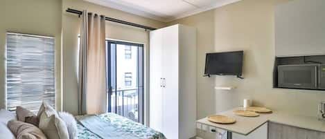 A bedroom with a bed, a bedside table with a microwave, a TV, and a wardrobe.