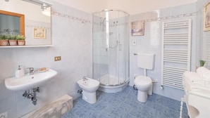 A bathroom with a glass-enclosed shower, a sink, two bidets, and a toilet.