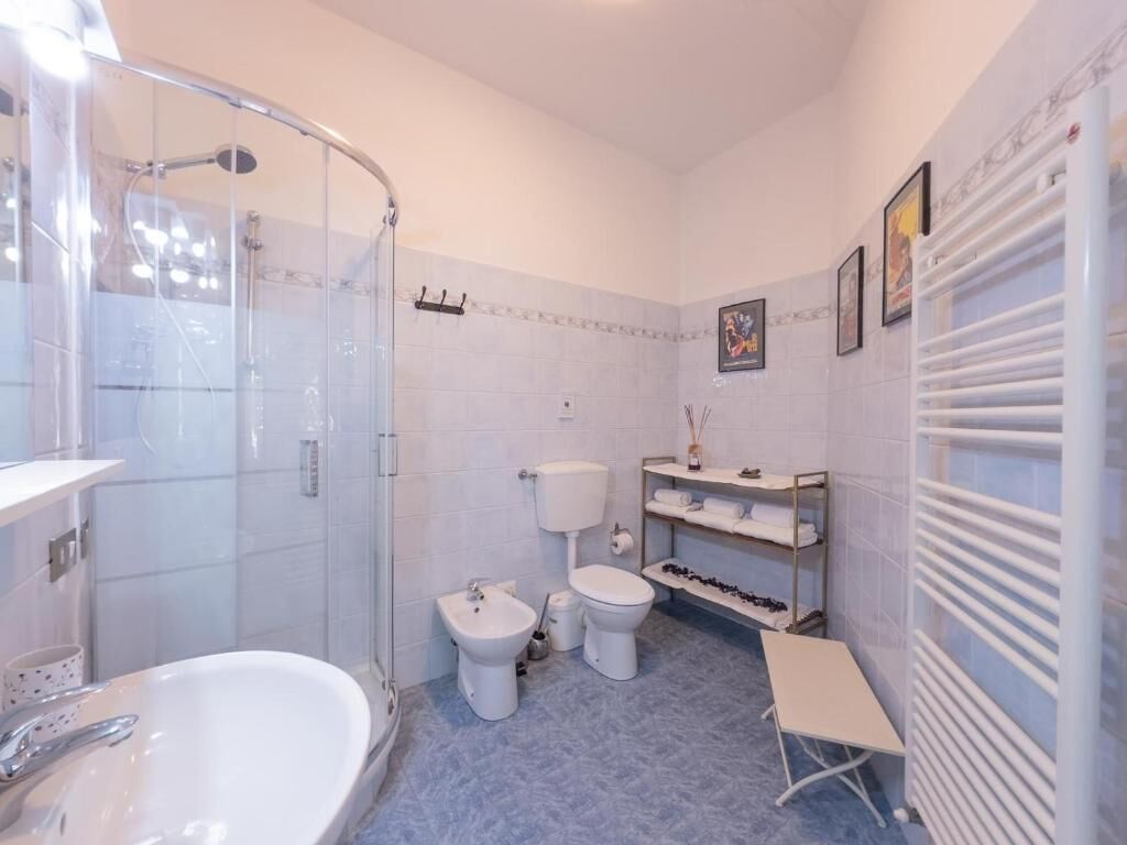 A bathroom with a glass-enclosed shower, a bathtub, a sink, two toilets, and a towel rack.