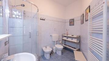 A bathroom with a glass-enclosed shower, a bathtub, a sink, two toilets, and a towel rack.