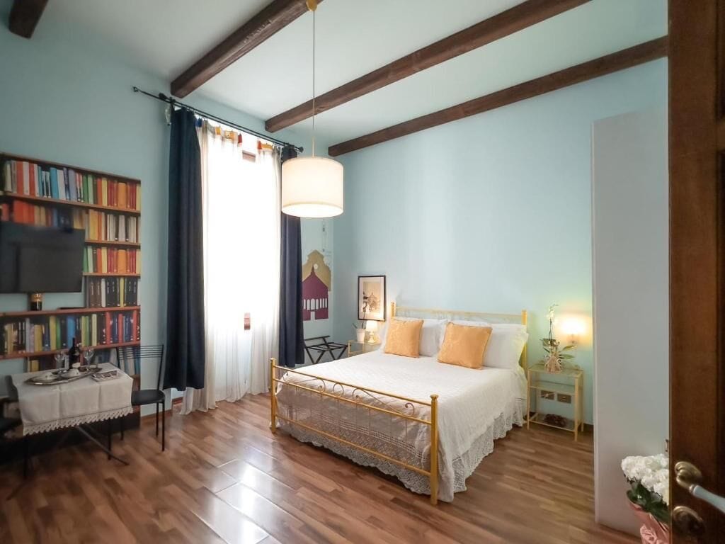 Een slaapkamer met een houten bed, een boekenkast, een eettafel en een raam met gordijnen.