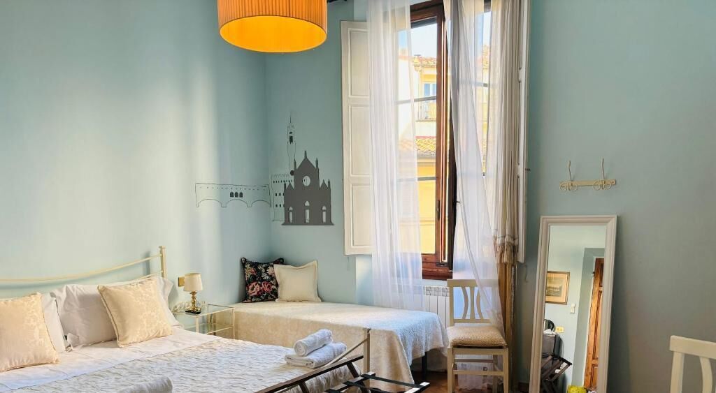 Une chambre avec deux lits, une fenêtre avec des rideaux, un miroir et une œuvre d’art accrochée au mur.