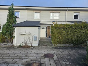A residential building with a front door, a small shed, and a hedge.