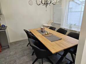 A dining area with a wooden table, black chairs, a chandelier, a clock, and a window with blinds.