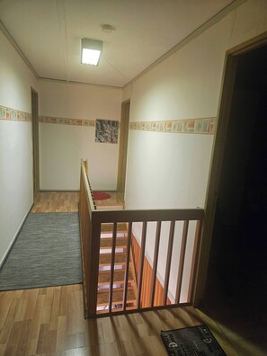 Un escalier avec une rampe en bois menant à l’étage supérieur, un petit tapis au pied de l’escalier et un tableau accroché au mur.