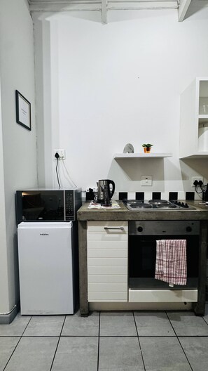 A compact kitchenette with a refrigerator, microwave, stove, and a small shelf above the counter. - Experience Elevated Living in Dainfern's Panorama Suite (Sandton)