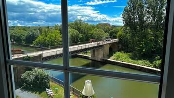 Blick auf einen Fluss mit einer Brücke, einer Außenbestuhlung und Grünflächen.