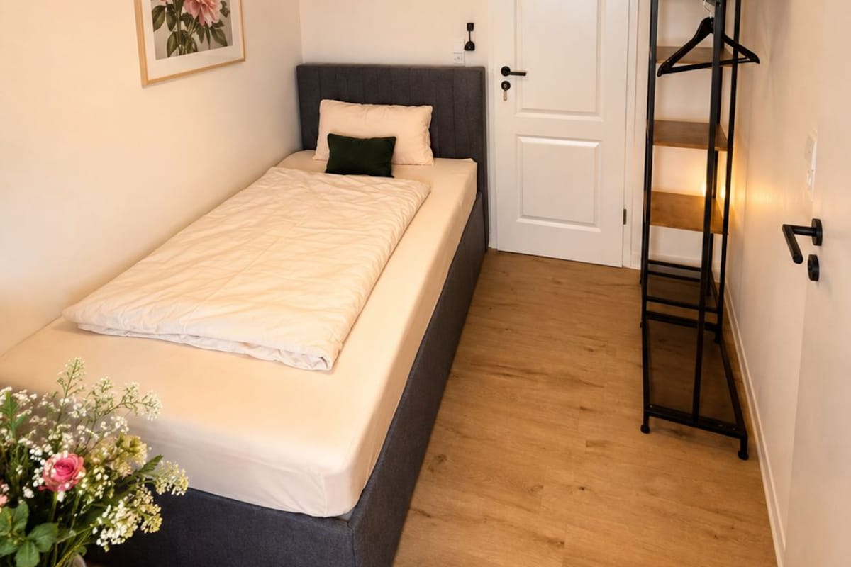 A bedroom with a bed, bedside table, and a wall-mounted shelf with a hanging rack.