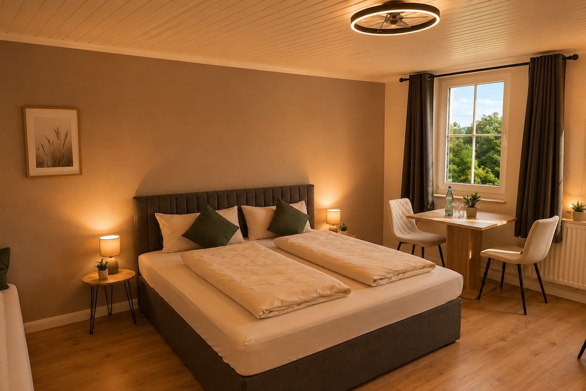 A hotel room with a large bed, bedside tables, a desk, and a view of greenery outside.