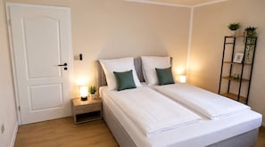 A bedroom with a double bed, bedside tables, a nightstand, a door, and a wall-mounted shelf with plants. - Hotel NeckarOase (Lauffen am Neckar)
