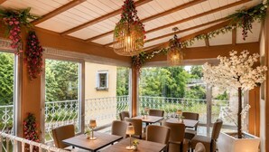 An indoor dining area with tables and chairs, a balcony with a railing, and decorative plants.