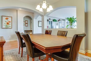 A dining room with a rectangular table, six chairs, a chandelier, and a large window with a plant. - Modern Home w/ Private Deck & Yard in Indianapolis (Indianapolis)