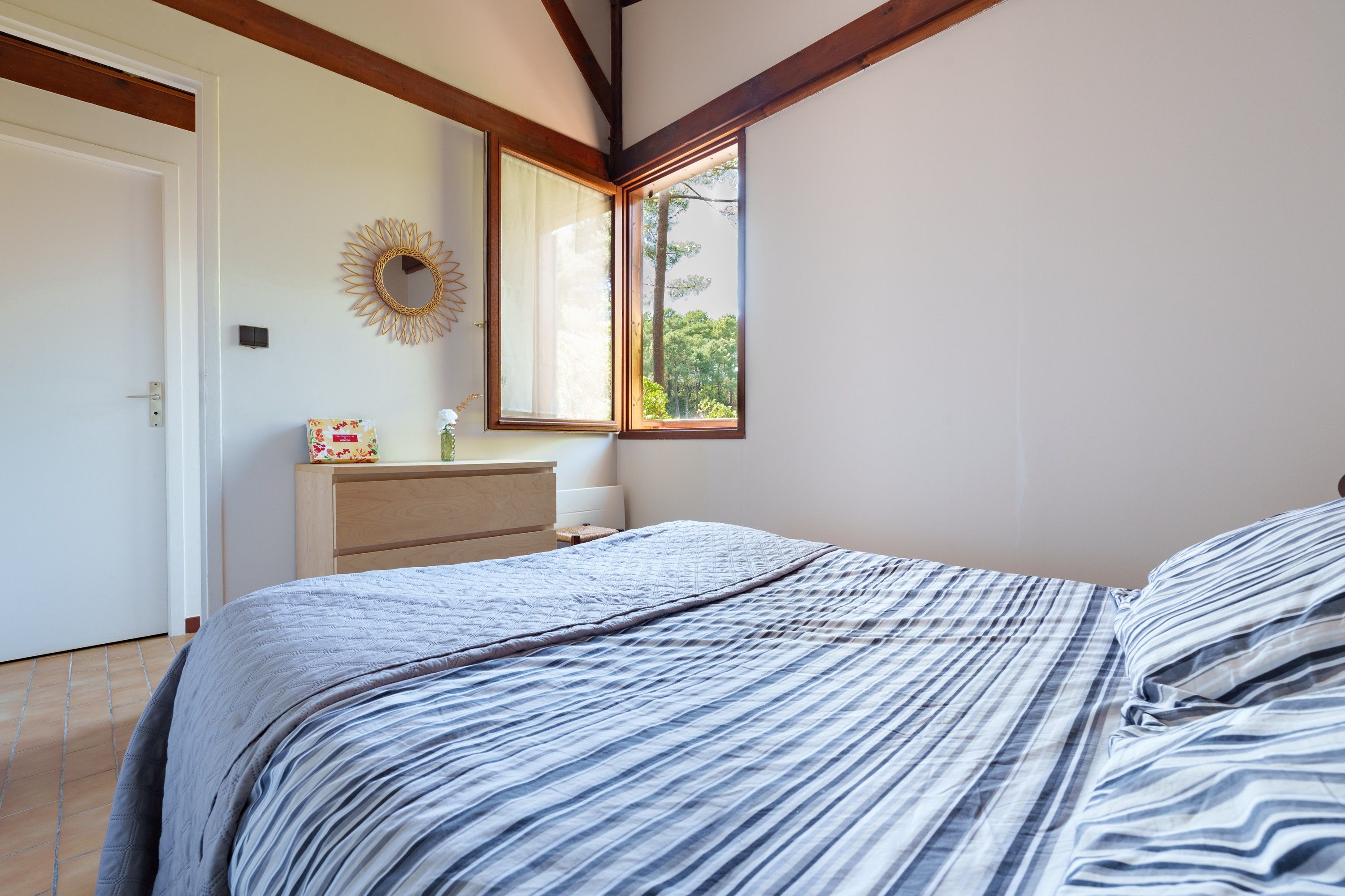 A bedroom with a bed, a dresser, a mirror, and a window with a view of trees.