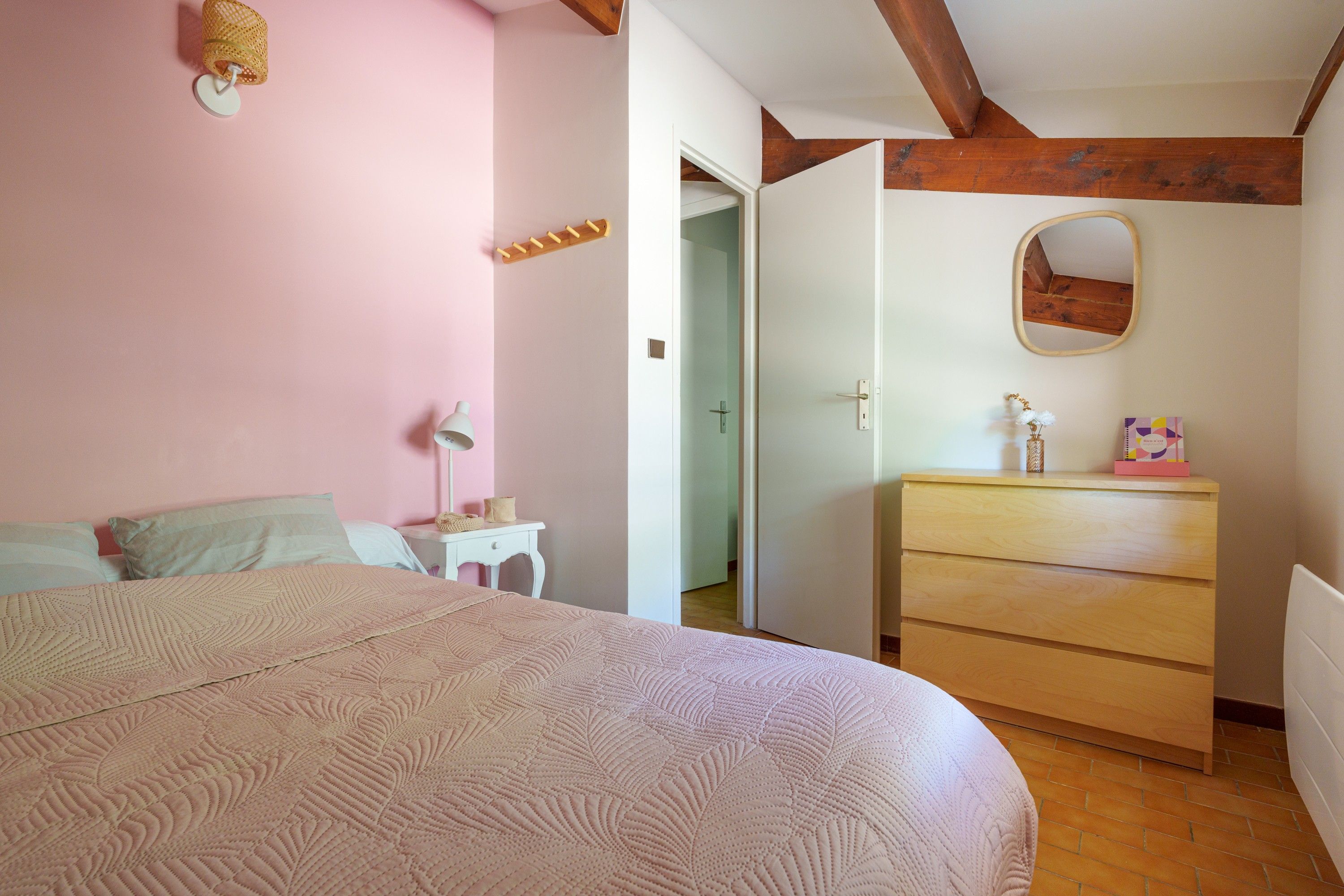 A bedroom with a bed, bedside table, dresser, and a mirror on the wall.