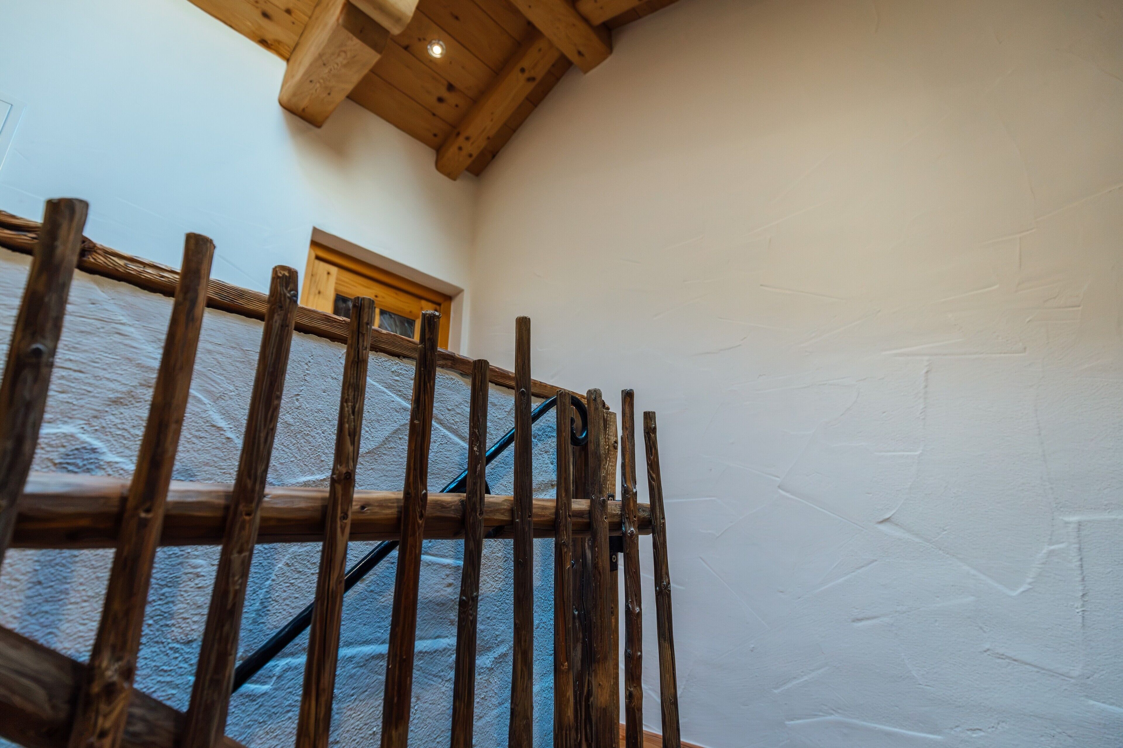 Una scala in legno con ringhiera metallica che conduce a una stanza con soffitto in legno e una finestra.