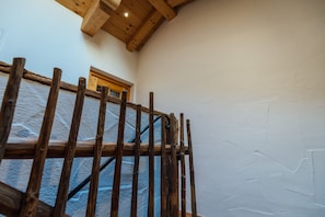 A wooden staircase with a metal handrail, leading to a room with a wooden ceiling and a window.
