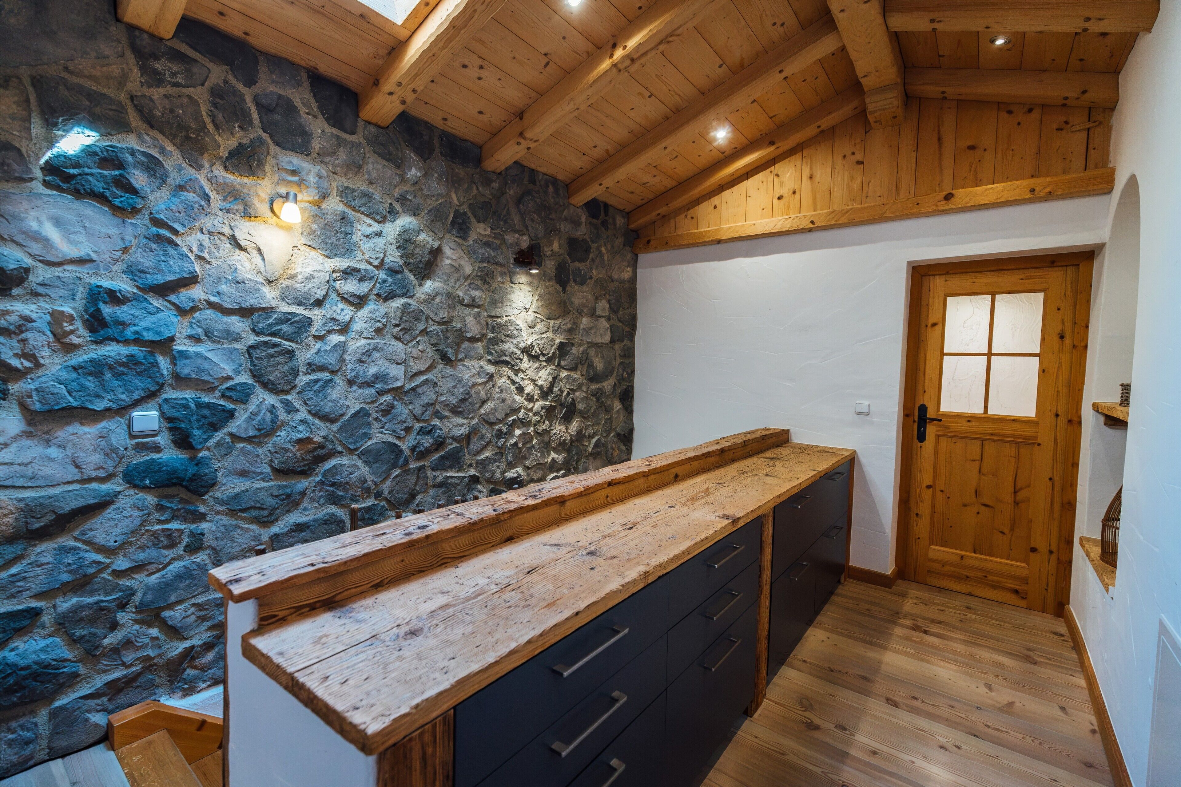 Una habitación con pared de piedra, vigas de madera en el techo, un mostrador de madera y una puerta con paneles de vidrio esmerilado.