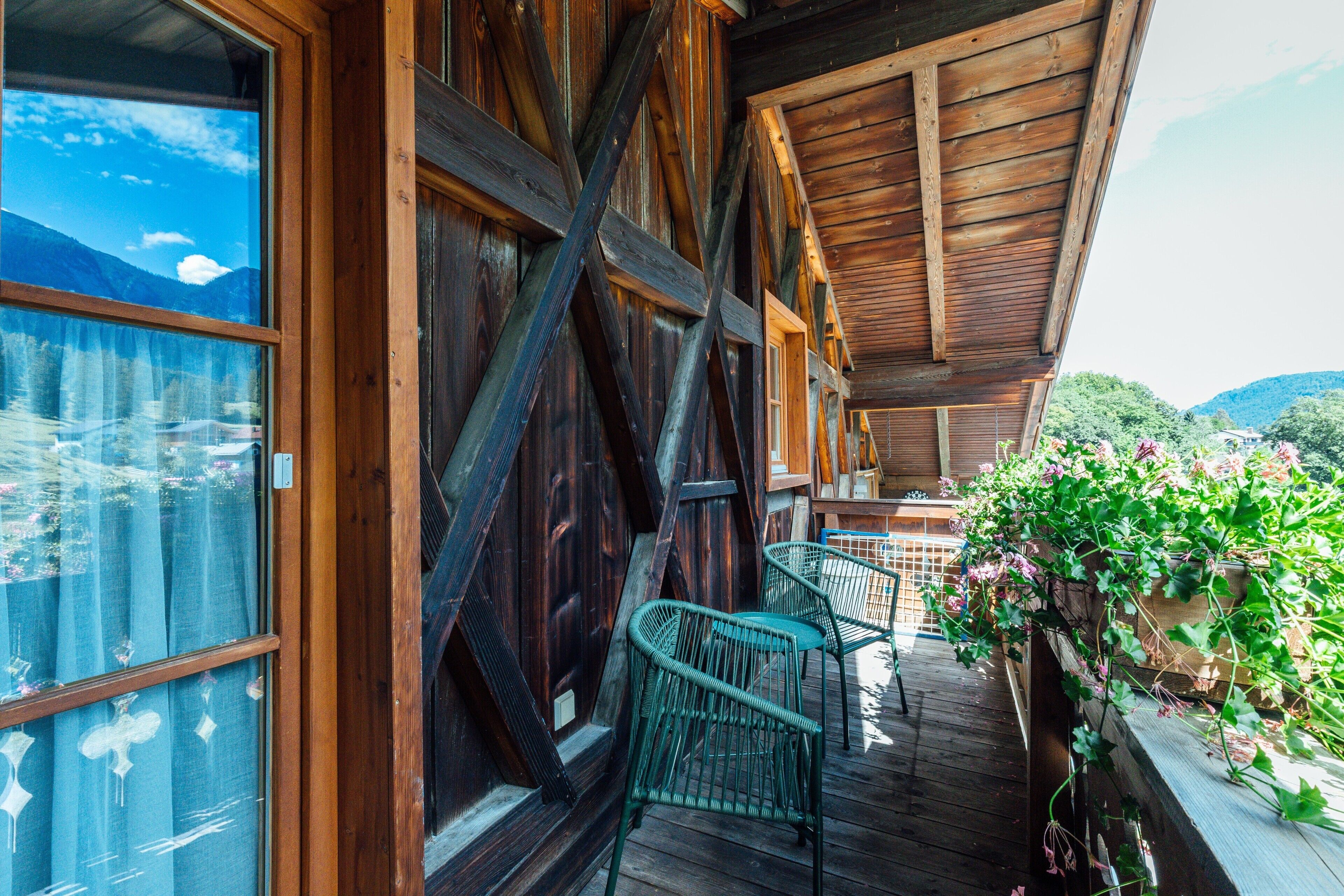 Un balcone in legno con vista sulle montagne, due sedie in vimini e una ringhiera di legno.