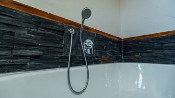 Eine Badewanne mit Duschkopf und Brause, vor einer Steinwand mit Holzverkleidung.