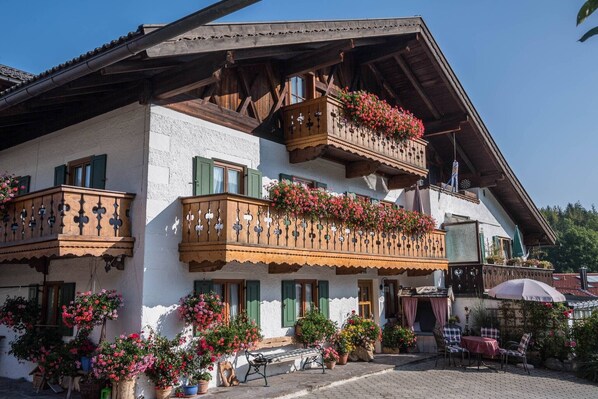 A traditional chalet with wooden balconies adorned with flowers, a paved courtyard, and outdoor seating.