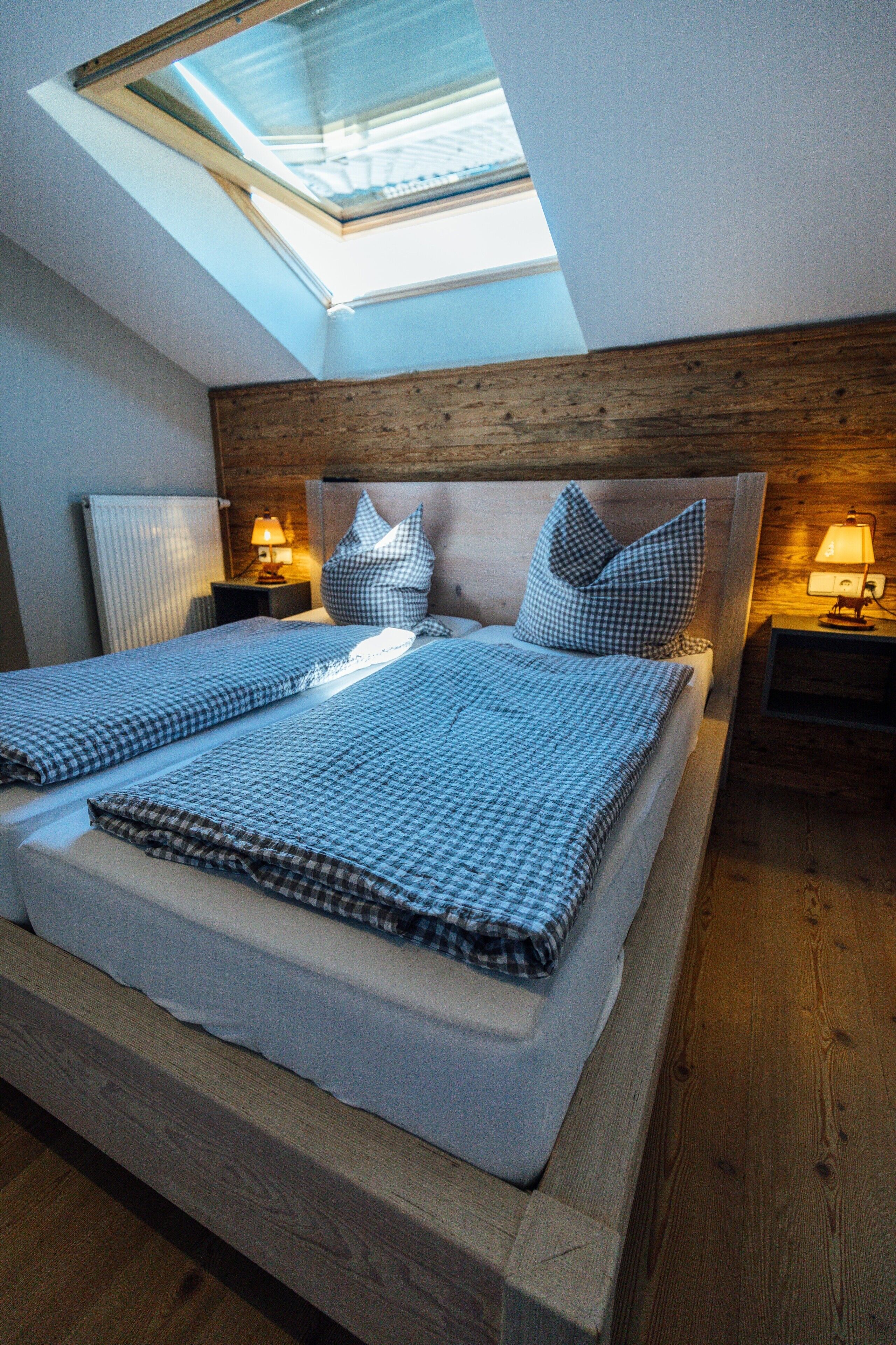 Ein Schlafzimmer mit Oberlicht, einem Bett mit Karomuster-Bettwäsche, zwei Nachttischlampen und einem Holz-Kopfteil.