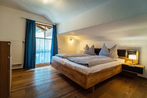Un dormitorio con una cama de madera, una mesita de noche con lámpara y vistas a través de una ventana con cortinas.