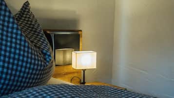 Een bed met een geruit sprei en een kussen, een nachtkastje met een lamp, en een spiegel aan de muur.
