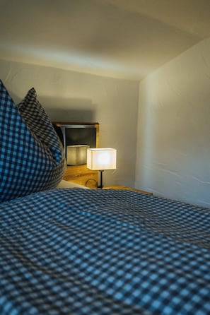 A bed with a checkered bedspread and a pillow, a bedside table with a lamp, and a mirror on the wall.