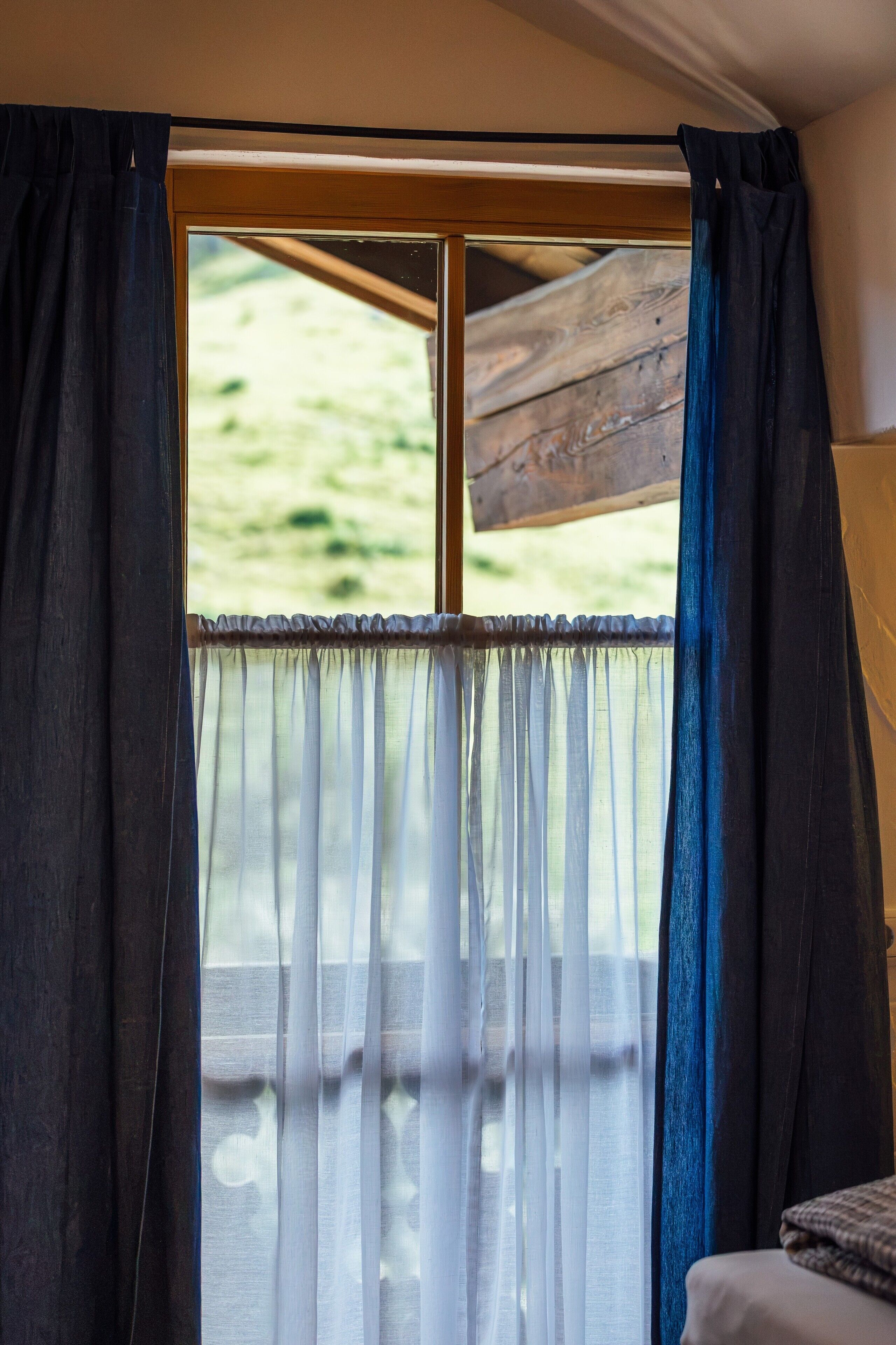 Ein Zimmer mit einem Fenster, das mit schweren, dunklen Vorhängen und durchsichtigen weißen Vorhängen drapiert ist.