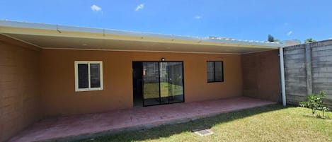 A covered patio area with a sliding glass door, a small window, and a concrete wall.