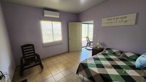 Un dormitorio con cama, una silla, una ventana con persianas, una puerta y un letrero en la pared.