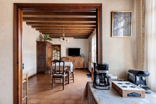 A cozy kitchen with a wooden ceiling, a dining table with chairs, a coffee machine, and a television.