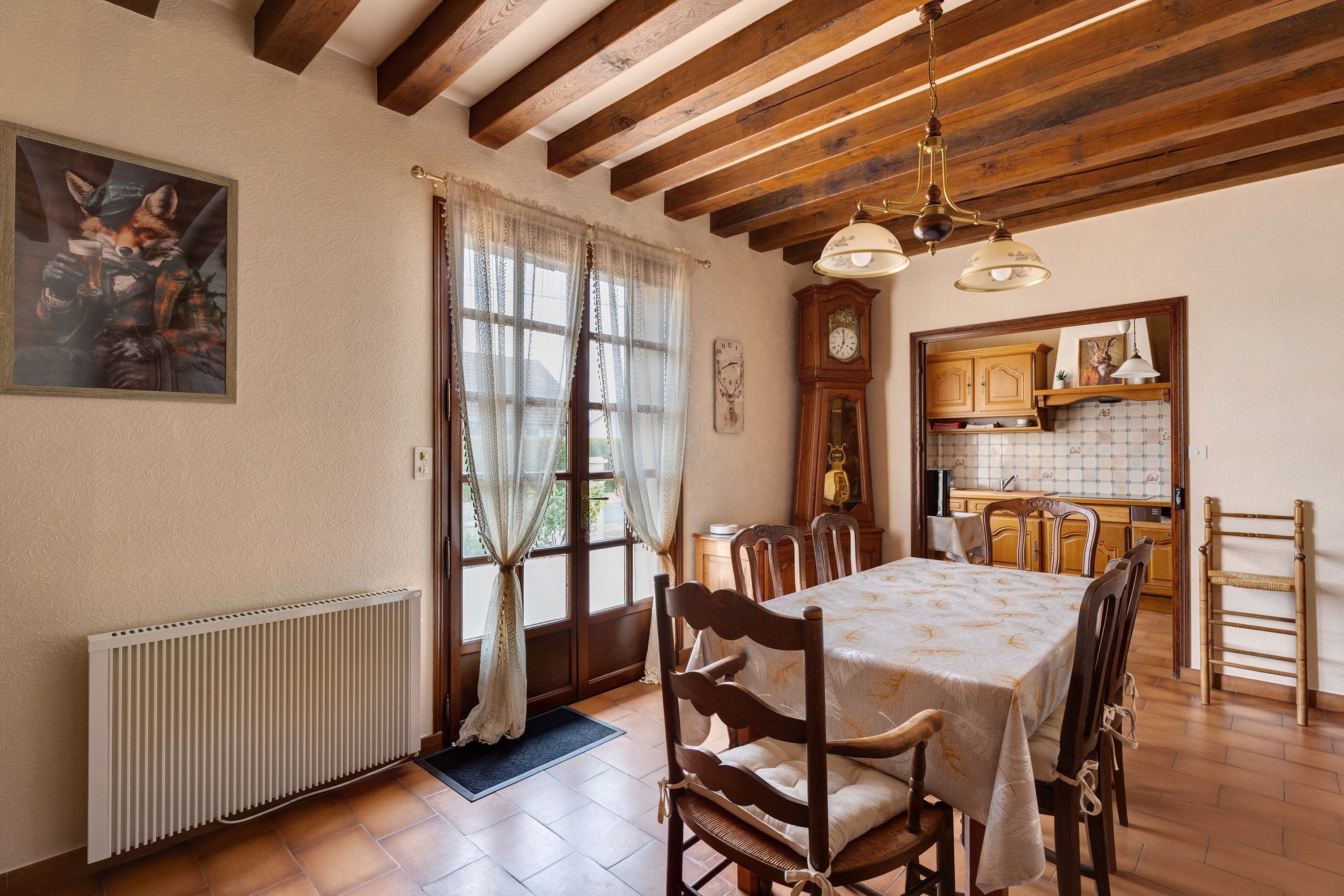 Una sala da pranzo con un tavolo e sedie in legno, un termosifone e una finestra con tende.